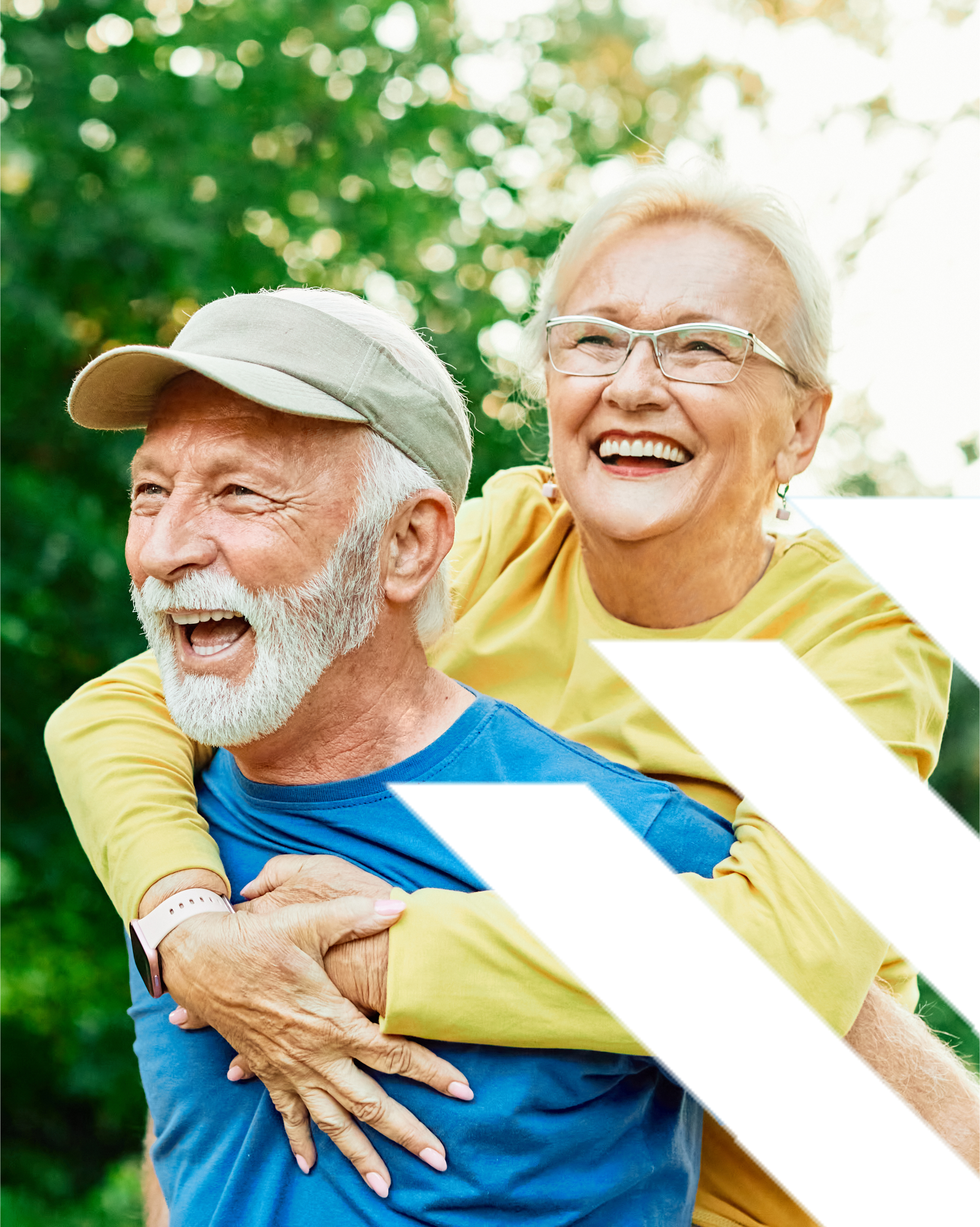 Older couple embracing and smiling at the beach on a sunny day, showing warmth and companionship with a clear blue sky behind them.